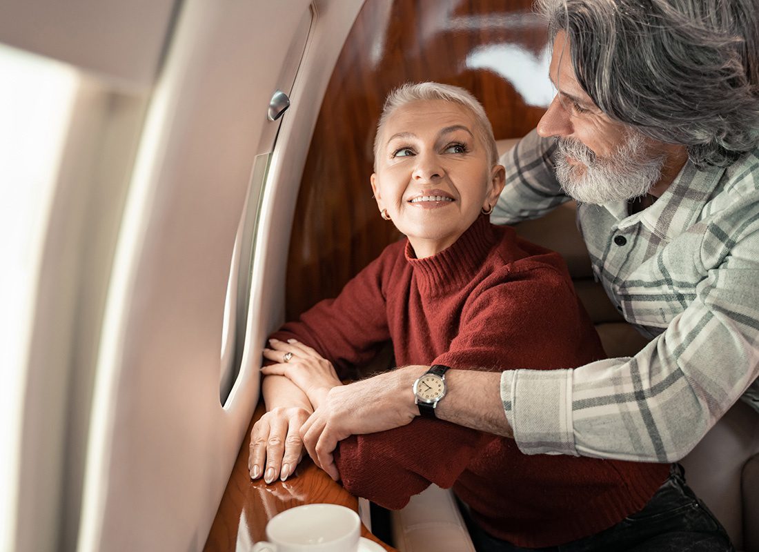 We Are Independent - Portrait of a Smiling Elderly Couple Wearing Sweaters Sitting Next to the Window on a Private Jet