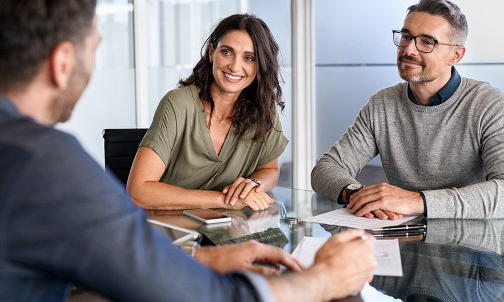 Blog - Couple Smiling and Sitting with an Insurance Agent at His Office on a Nice Day
