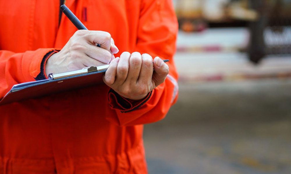 An On-Site Risk Visit May Save You From A Violation - Worker In Uniform Filling Out A Document On A Clipboard
