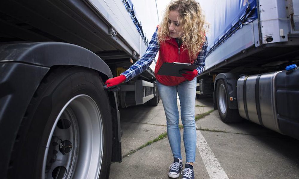 Driving Safety and Health Tips for Truck Drivers - Woman checking the tires on a truck with a clipboard