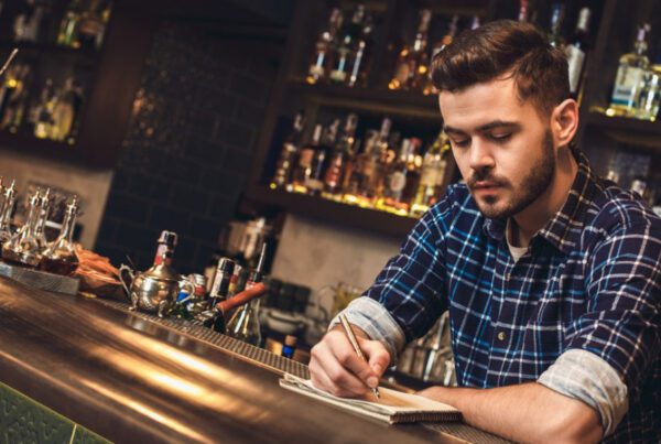 Blog - Bartender Behind a Bar Writing in a Notepad and Focused