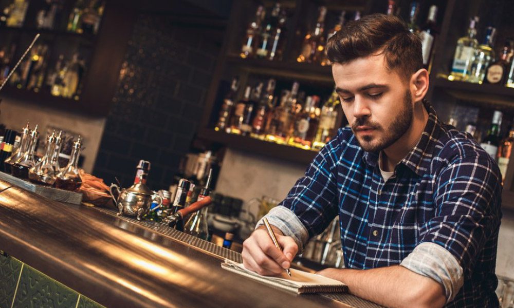 Blog - Bartender Behind a Bar Writing in a Notepad and Focused