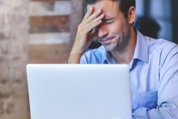 Blog - Business Man With Hand on Face Frustrated Sitting in Front of an Open Laptop