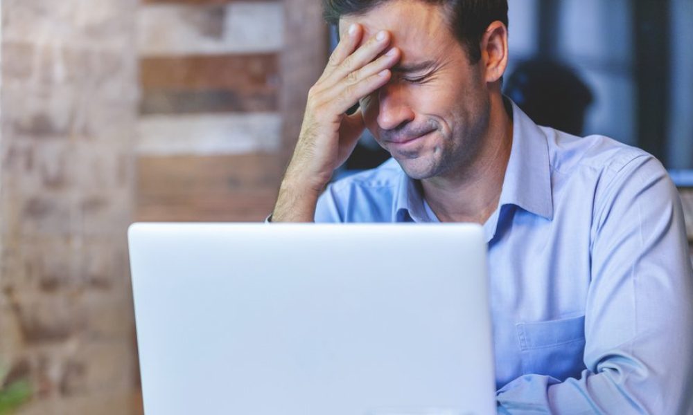 Blog - Business Man With Hand on Face Frustrated Sitting in Front of an Open Laptop